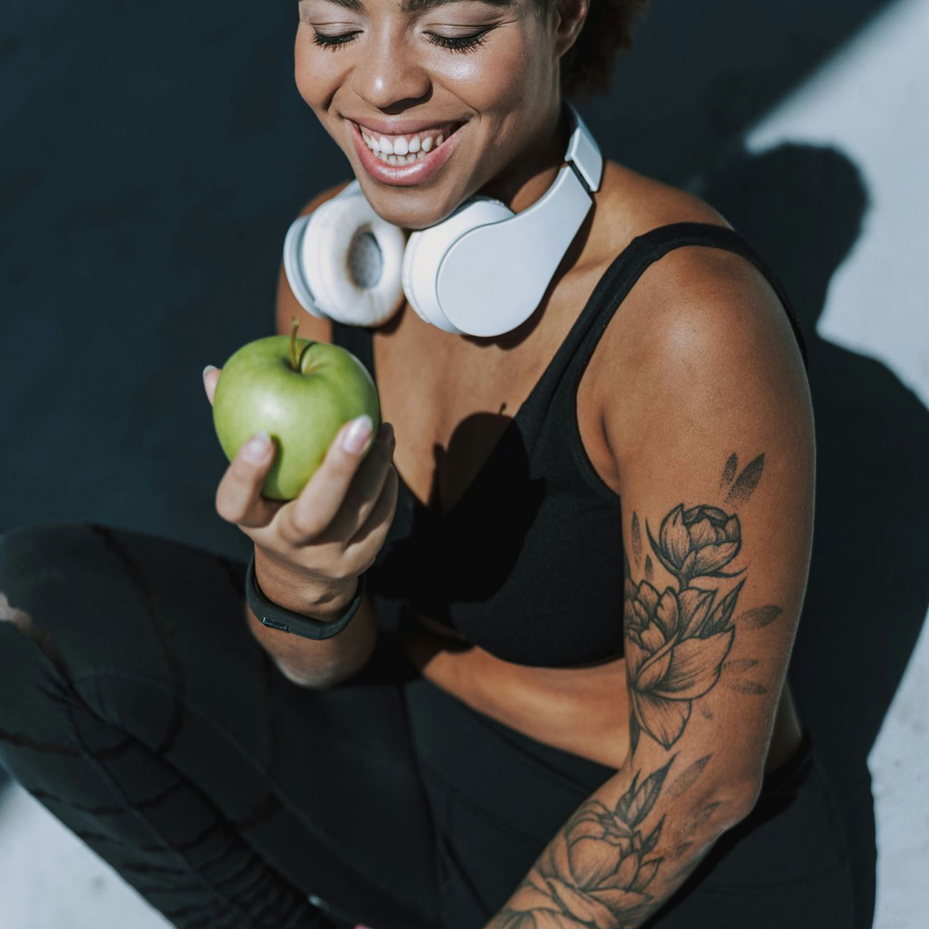 Woman in workout gear and headphones eating a green apple 