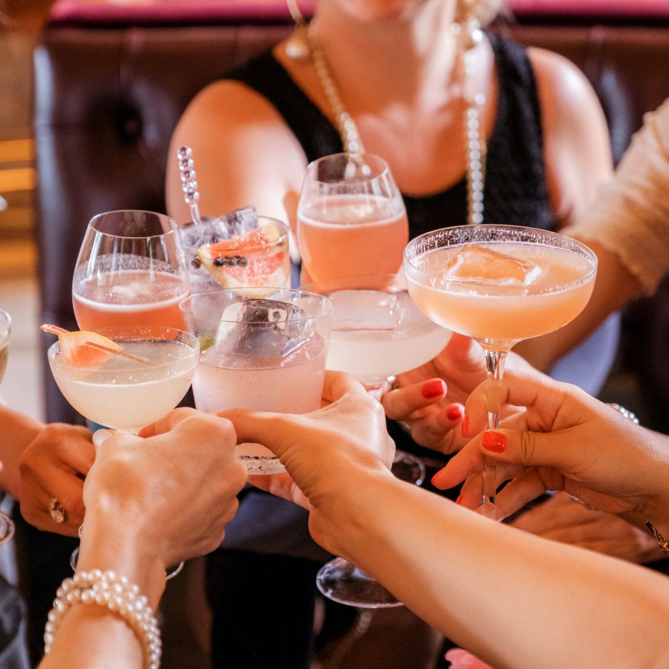 Close up of women's hands holding pink and clear cocktails during a toast.